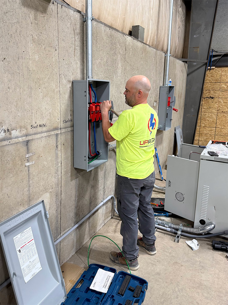 Upright Electric technician working on an open disconnect mounted on a concrete commercial wall