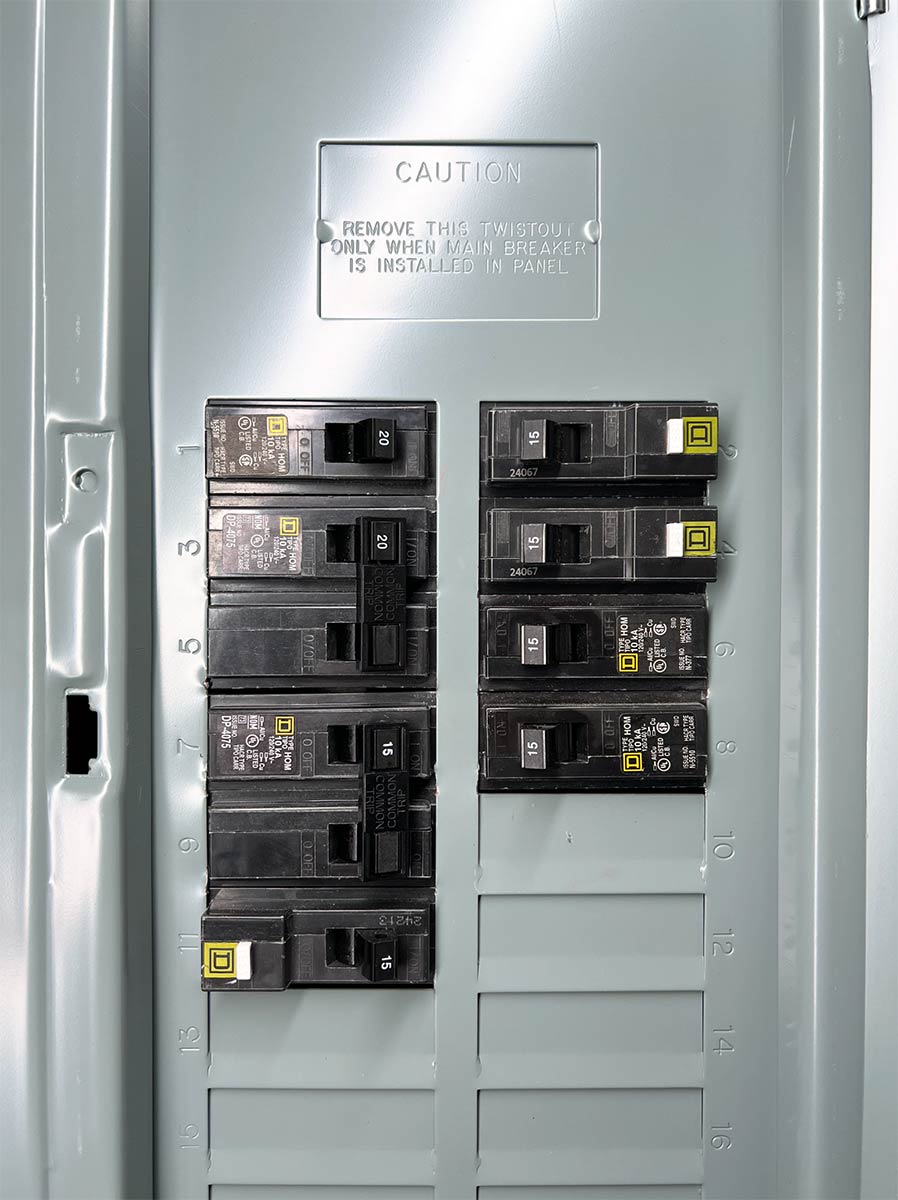 Open residential electrical panel with the cover removed, showing labeled breakers and the caution plate for the main breaker knockout