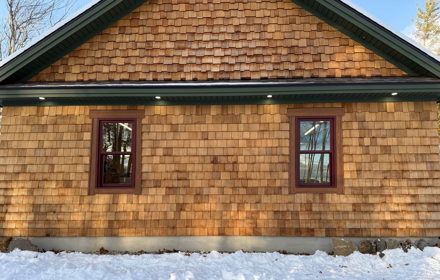 Cedar-shingle house with recessed soffit lighting after a snowfall in New Hampshire